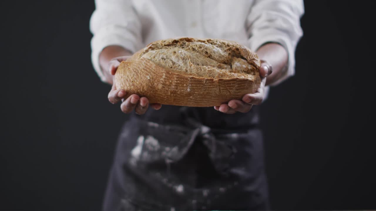 Video of cook holding loaf of bread on black background
