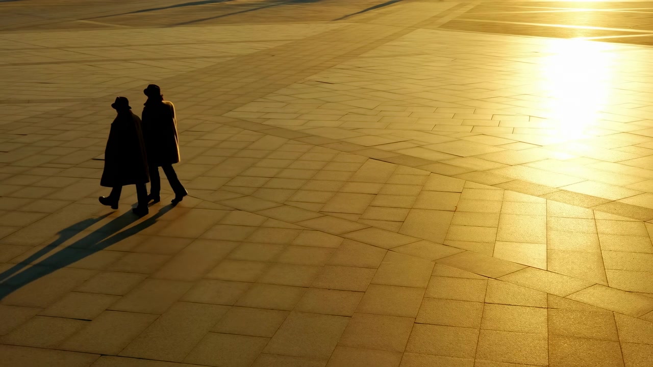 Two individuals stroll together on a tiled surface, bathed in sunlight, creating a peaceful and serene moment during their journey. The scene is set against a backdrop of warm, sun.