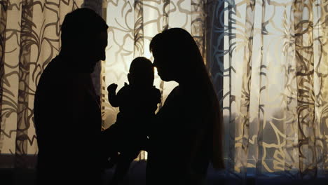 silhouette of a happy family are the house by the window at sunset gently hold the child in your arm