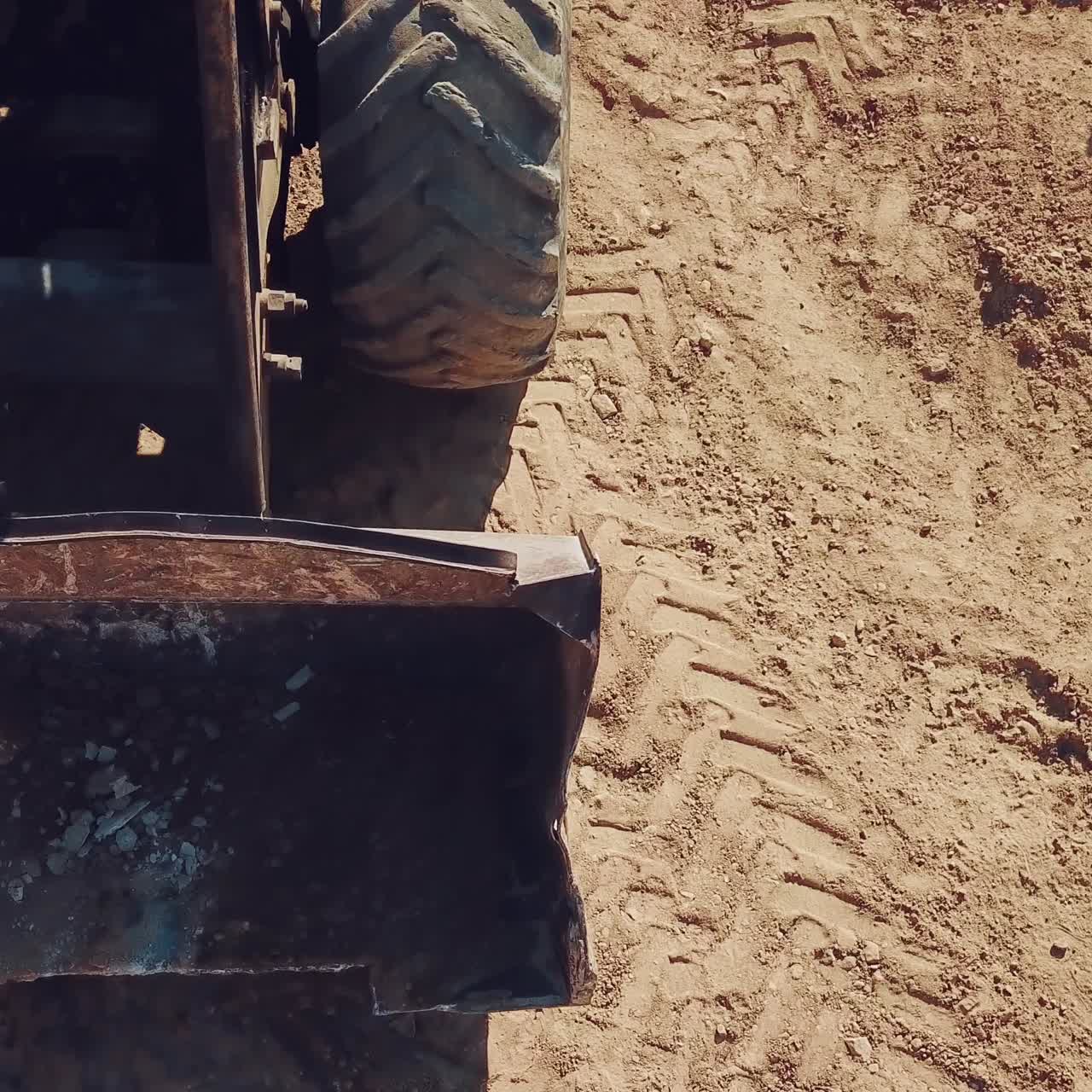 bulldozer with huge wheels and a bucket is moving around the territory of a sandy quarry. Close-up