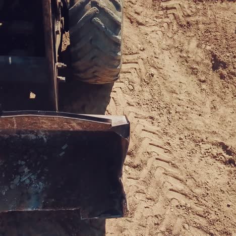 bulldozer with huge wheels and a bucket is moving around the territory of a sandy quarry. close-up