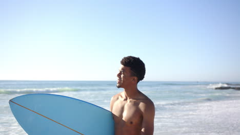 a young biracial man holds a blue surfboard at the beach with copy space