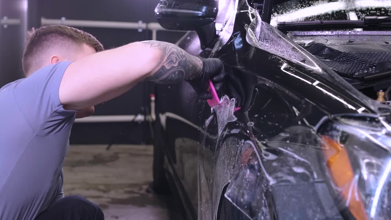 hombre que cubre el coche con cinta de poliuretano de vinilo. películas para el coche. pegatina película protectora en el coche