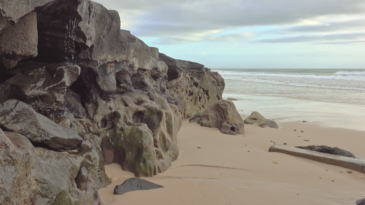el agua se filtra desde la roca negra de la playa hacia la arena y hacia el océano