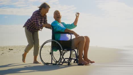 vista lateral de una pareja caucásica senior activa tomando una selfie con un teléfono móvil en la playa 4k