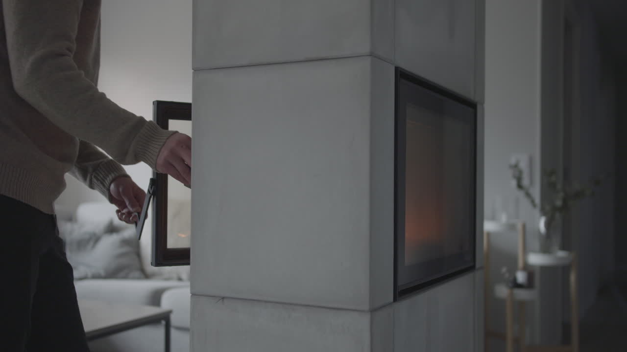 Man puts log into fireplace at Scandinavian home living room