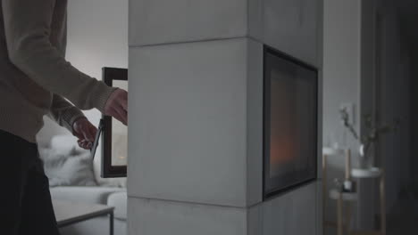 Man-puts-log-into-fireplace-at-Scandinavian-home-living-room