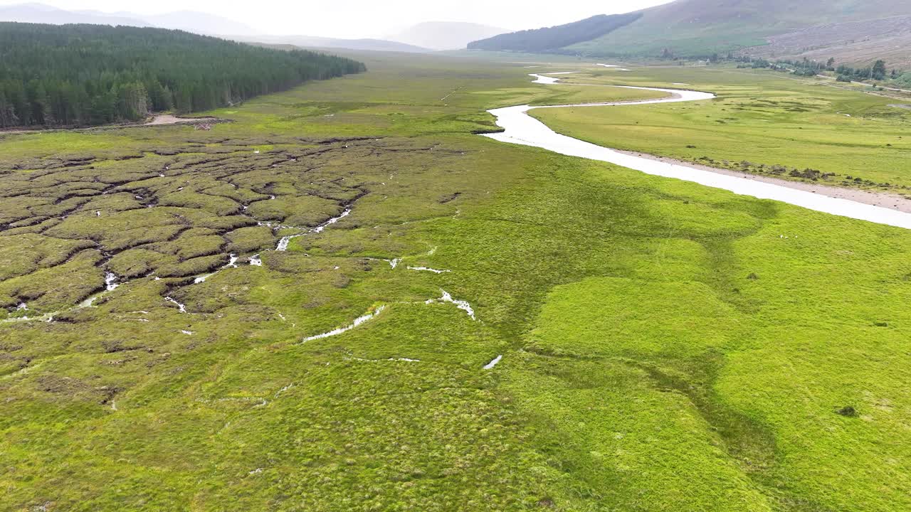 Drone glides above lush moorland, winding river, and wetlands under soft daylight in Fife