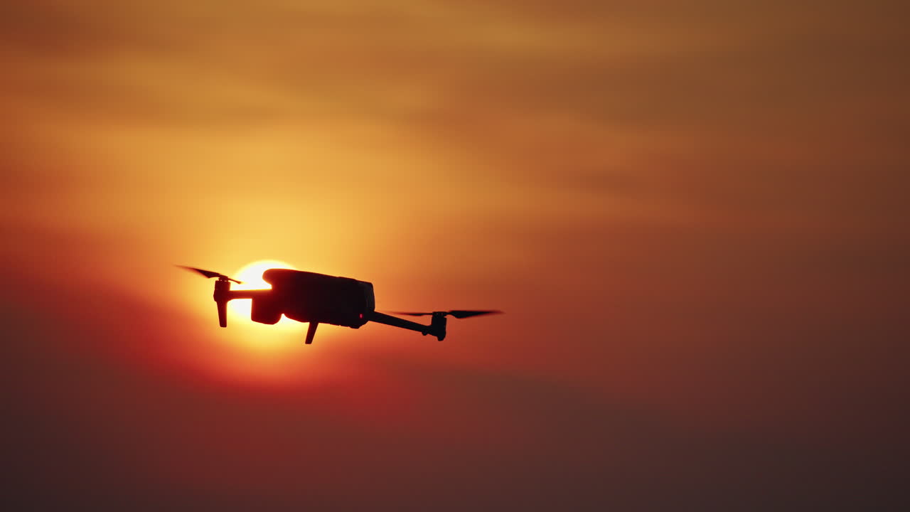 Drone flyver ind i billedet og manøvrerer foran en strålende solnedgang med orange himmel.