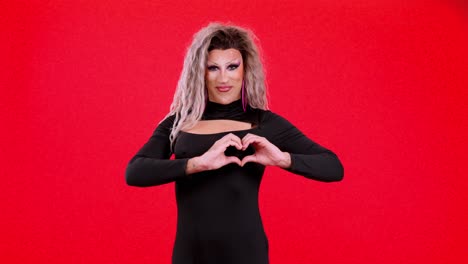 drag queen making a heart shape with hands on red background