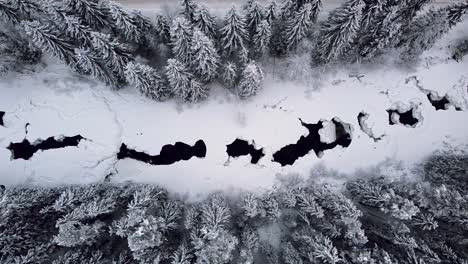 Imágenes-Aéreas-De-Drones-De-Un-Bosque-Cubierto-De-Nieve-En-Noruega,-Que-Revelan-Un-Río-Parcialmente-Congelado-Que-Serpentea-A-Través-Del-Prístino-Paisaje-Invernal