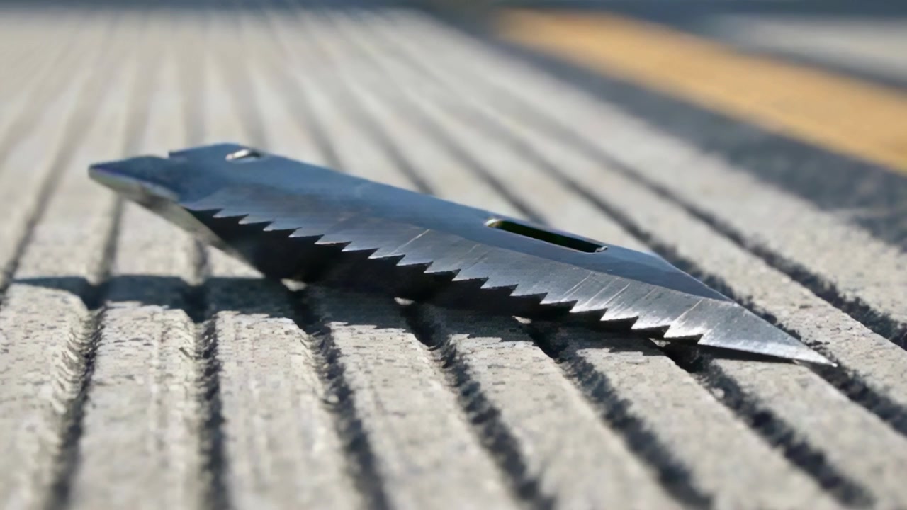 Shifting focus, camera zooming serrated blade on grooved concrete beside road stripe to show teeth