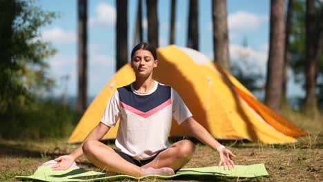 woman meditating in a forest near a tent