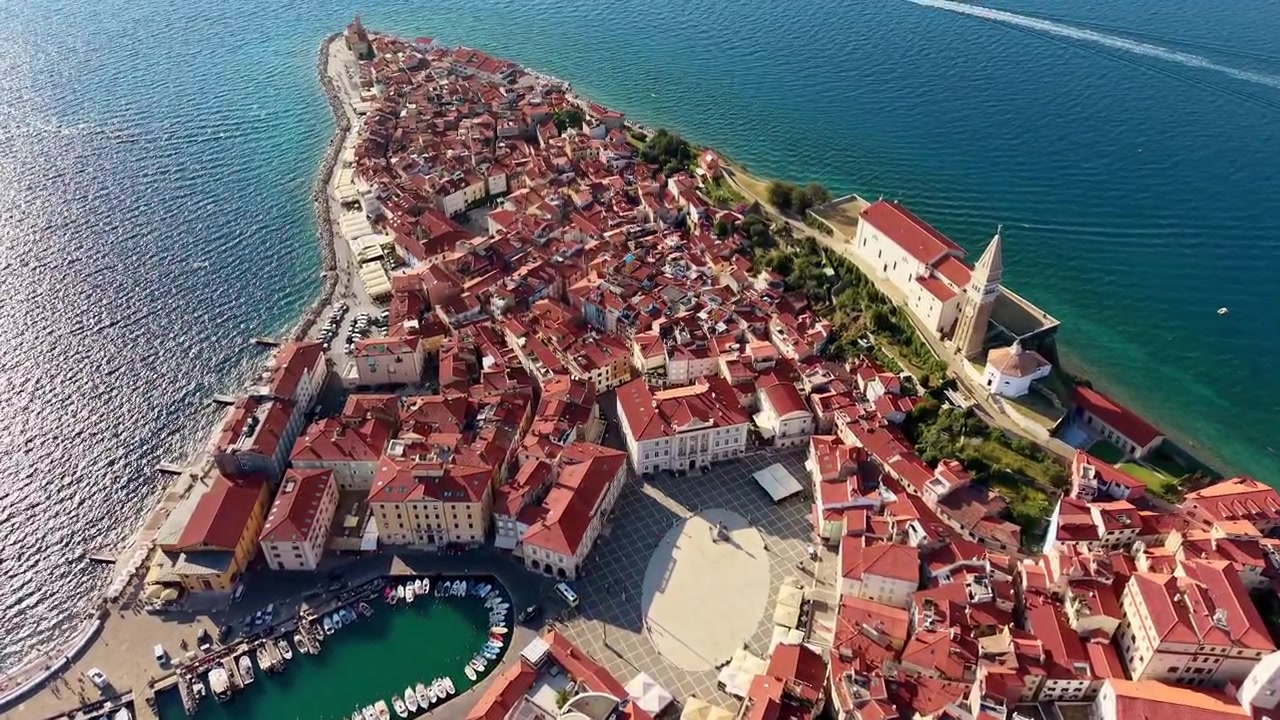 Veduta aerea con drone della piazza principale ovale, del porto e della chiesa sopra i tetti rossi del centro storico, Pirano, Slovenia