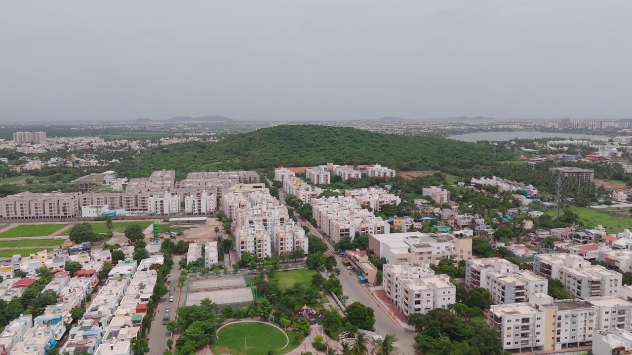 La periferia residenziale si estende verso una collina verde mentre il drone avanza su Chennai
