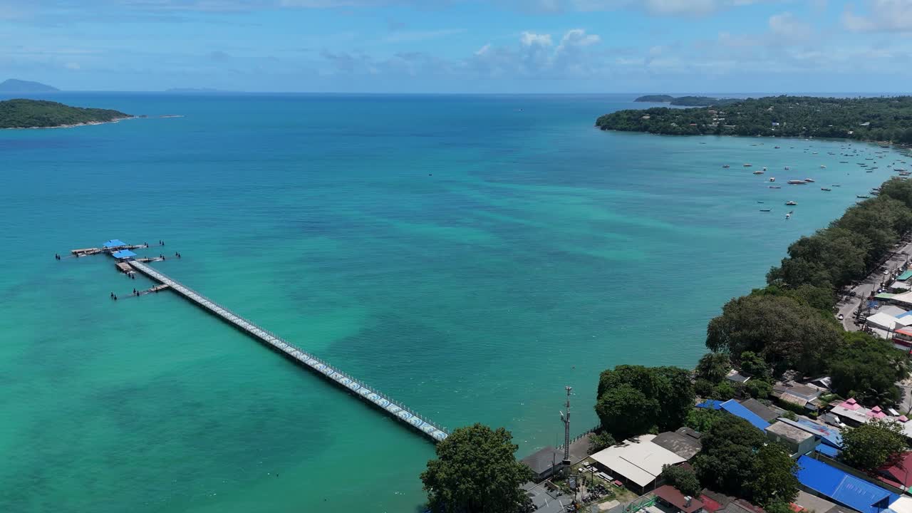 Drone pans a panorama over Rawai Beach, revealing the floating pier and turquoise sea
