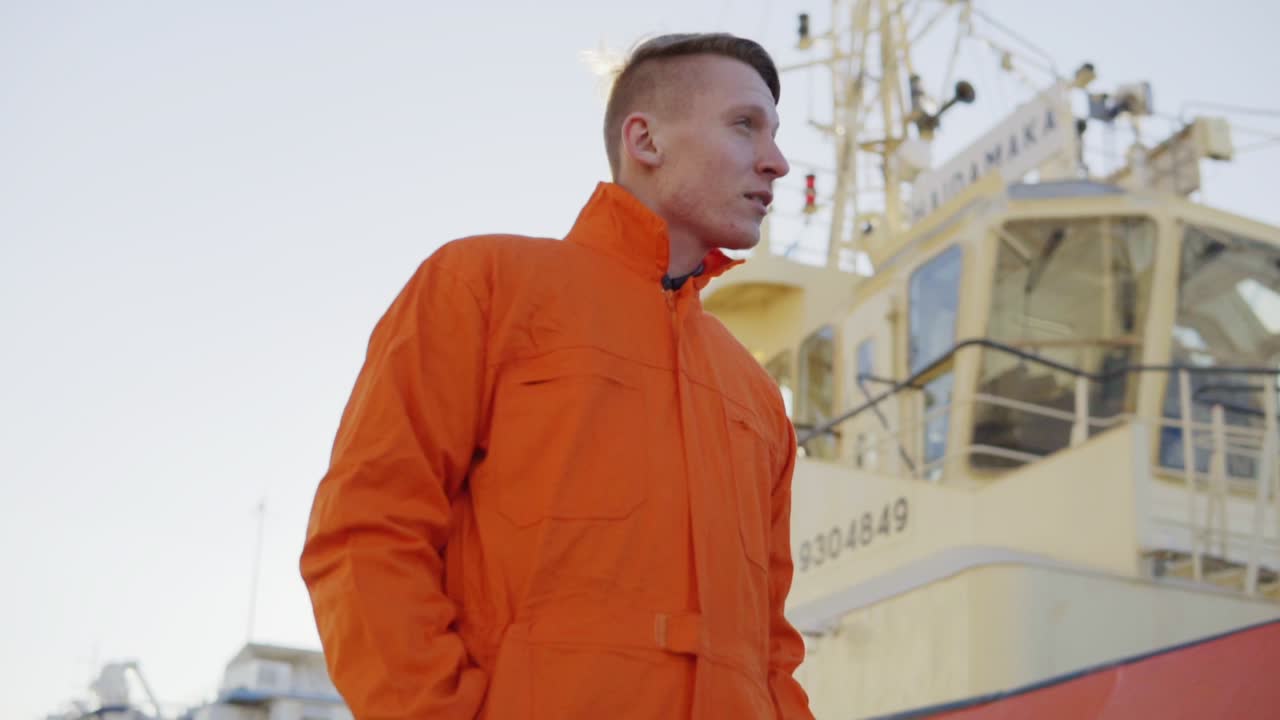 capitán del puerto en uniforme naranja de pie frente a un gran barco en el puerto y sonriendo