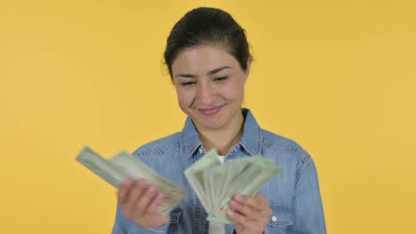 happy young indian woman counting dollars, yellow background