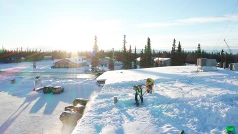 two men shoveling the snow off the roof of a local business warehouse in soldotna, alaska