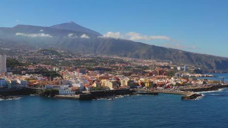 Vista-Panorámica-De-La-Ciudad-De-Puerto-De-La-Cruz,-Islas-Canarias,-España,-Su-Puerto-En-La-Costa-Del-Océano-Atlántico,-Debajo-De-La-Montaña-Pico-De-Teide,-Mar-Azul-Y-Cielo,-Toma-Aérea-De-Zoom-4k