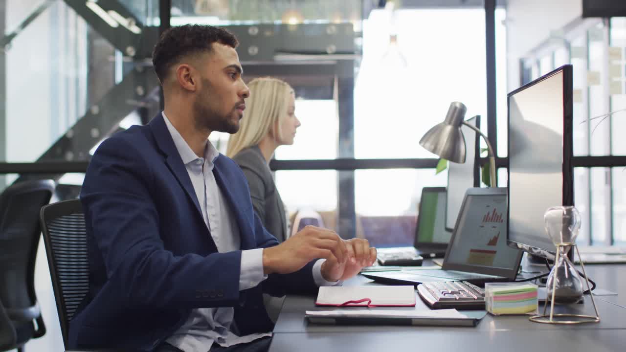 uomo d'affari di razza mista che usa il computer con un collega che lavora in background
