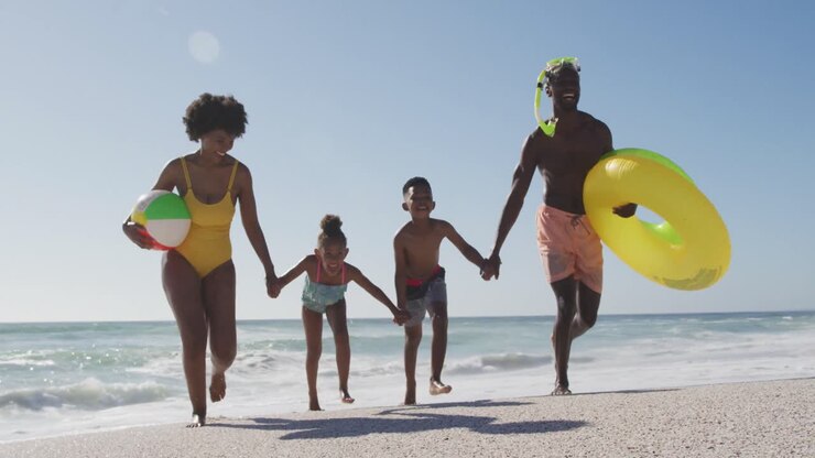 Famille afro-américaine souriante avec des objets gonflables courant sur une plage ensoleillée