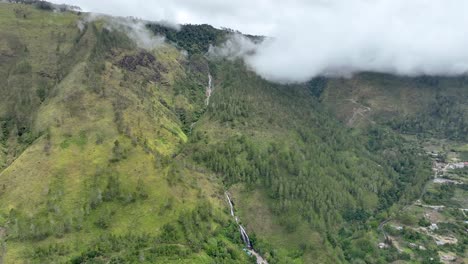 Efrata-waterfall-in-sumatra-with-clouds-shrouding-lush-green-mountains,-aerial-view