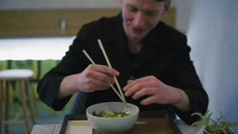 close up view of a man trying to eat noodles using chopsticks. learning how to hold chopsticks. noodles with vegetables. dinner