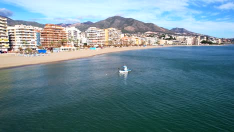 Aerial-dolly-across-fuengirola-hills-beach-with-small-tug-boat