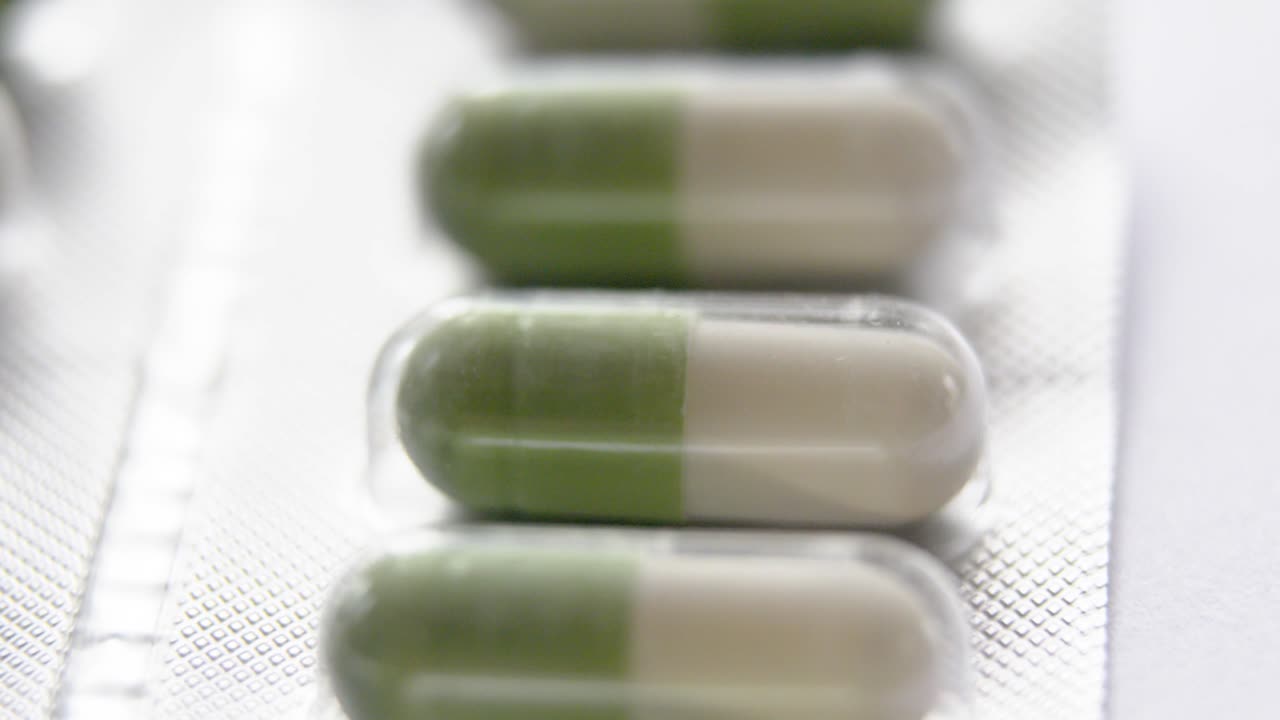 very bright vertical close-up from top to bottom of green and white capsules in their aluminium blister pack