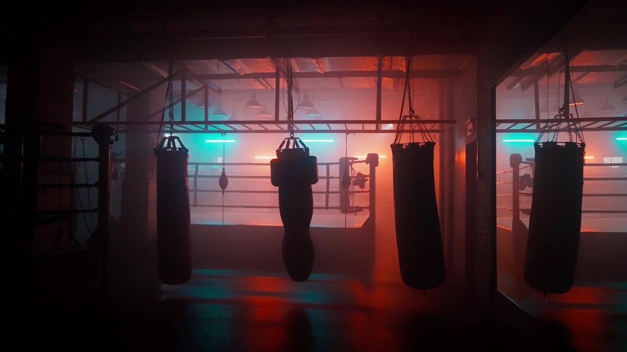 Interno di una palestra di boxe buia con sacchi da boxe e luci al neon