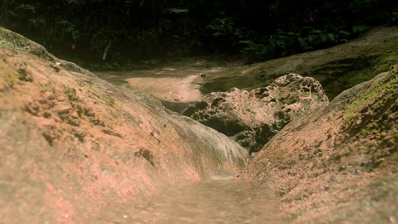 close up of crystal clear water running over yellow and moss covered rocks as sunlight shines off them in a rainforest in the Philippines.