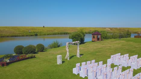 wedding-venue-with-arch-on-meadow-near-pond-aerial-view