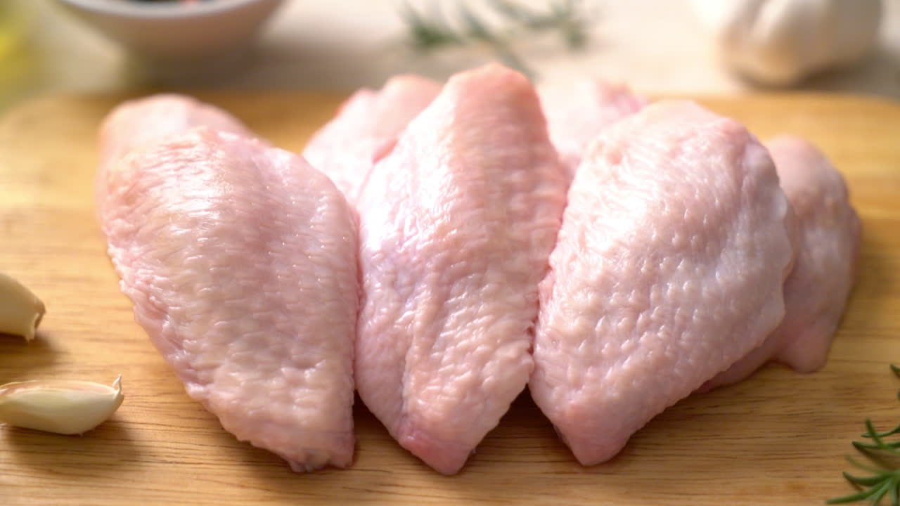 Alas de pollo medio crudo fresco sobre tabla de madera con ingredientes