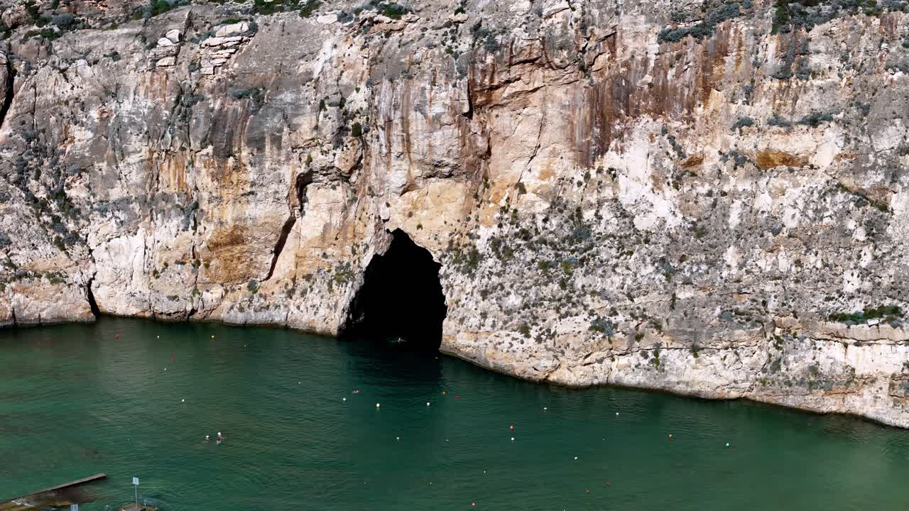 Espectacular toma amplia de la majestuosa entrada a la cueva del Mar Interior en Dwejra Gozo durante un día soleado de verano con acantilados de piedra caliza dorada reflejándose en las aguas turquesas del Mediterráneo bajo un cielo despejado.