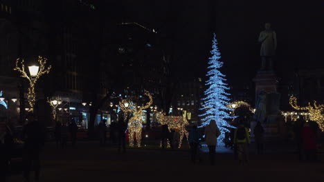 People-enjoy-Christmas-light-decorations-in-city-plaza-on-dark-night
