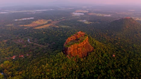 a breathtaking drone shot capturing the majestic sigiriya rock at sunrise, bathed in golden light and surrounded by misty forest.