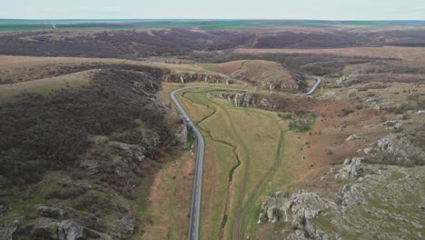 The-winding-road-through-dobrogea-gorges-with-surrounding-rocky-hills,-aerial-view