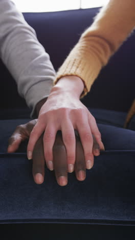 hands of diverse couple sitting on sofa in house, slow motion
