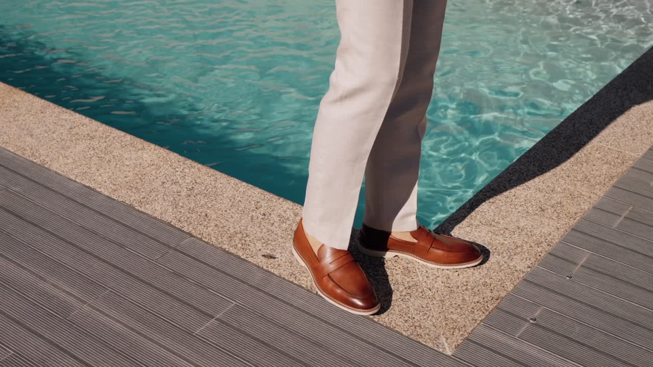 hombre en un traje beige de pie cerca de una piscina moderna con una cubierta de madera