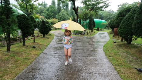 adorable little girl walking under rain holding yellow umbrella - tracking front view