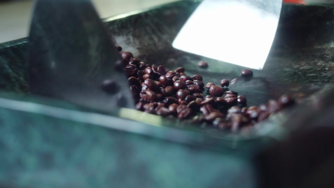 Primo piano della tostatura di chicchi di caffè con una spatola d'acciaio su una superficie di pietra verde. Processo di preparazione artigianale infuso con fuoco e liquore alle erbe in una caffetteria boutique.
