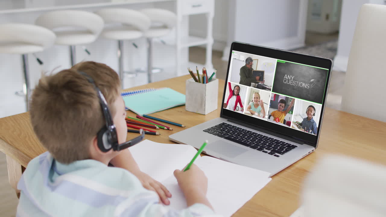 Schoolboy using laptop for online lesson at home, with diverse teacher and class on screen