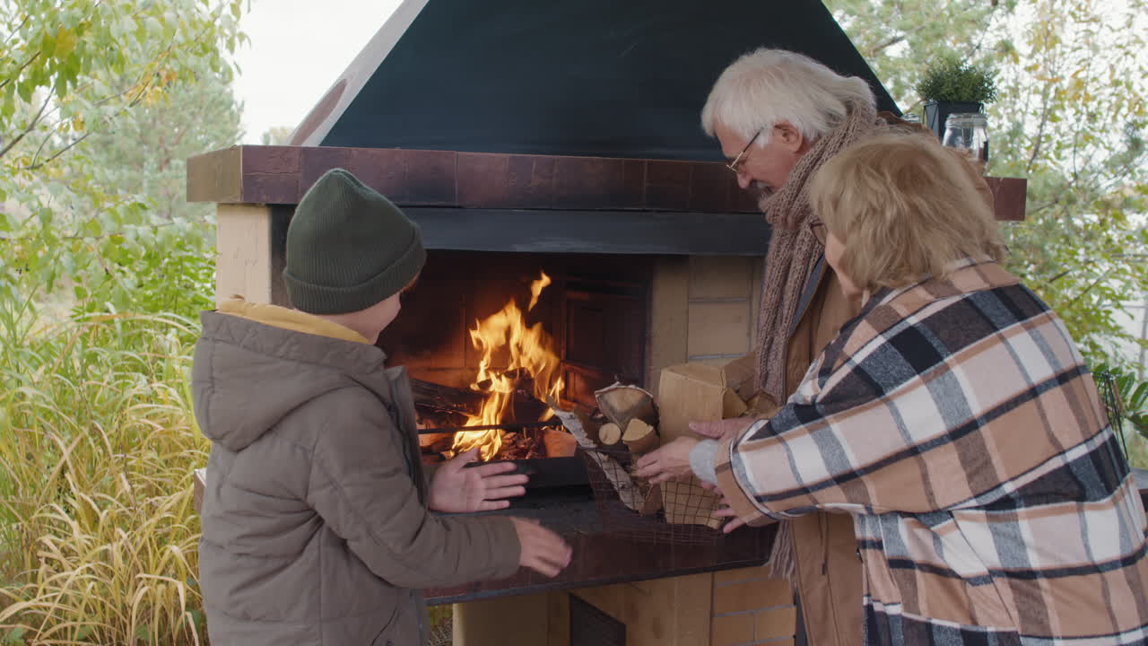 Child and Grandparents Kindling Fire in Outdoor Fireplace