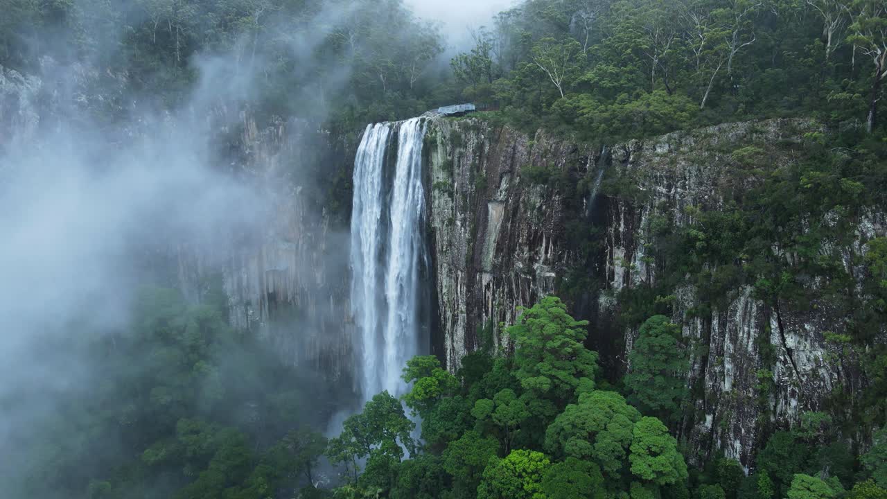 vista única de drones a través de una niebla suspendida que revela una majestuosa cascada que se derrama sobre un exuberante paisaje montañoso de selva tropical