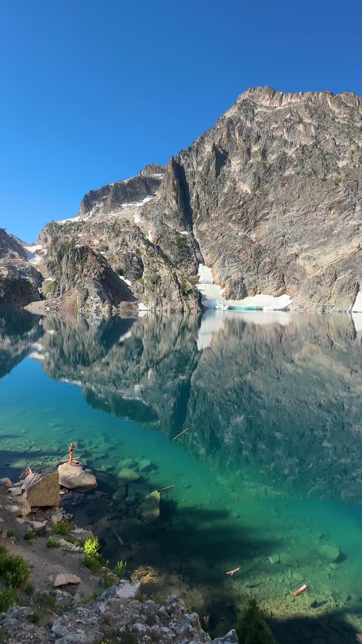 Vertical View, Amazing Emerald Alpine Lake Mirror Reflections and Woman in Bikini Standing on Rock
