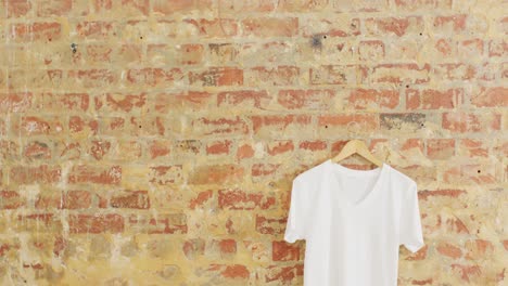 Video-of-close-up-of-white-t-shirt-hanging-on-brick-wall-background