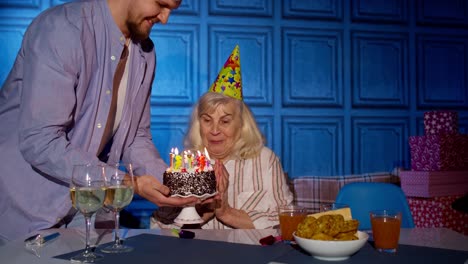 Große-Familie-Feiert-Den-Geburtstag-Der-älteren-Großmutter,-Wünscht-Sich-Etwas-Und-Bläst-Zu-Hause-Kerzen-An