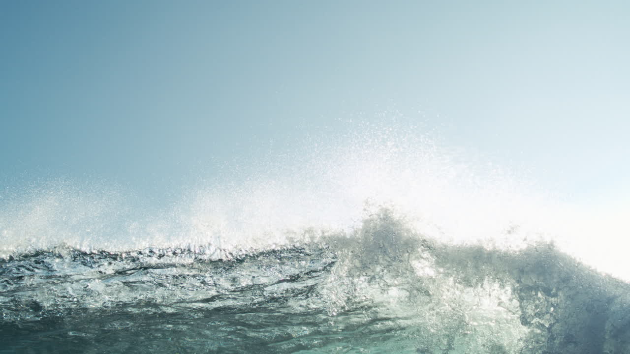 Slow motion wave rolling across open ocean with soft foam and sky above