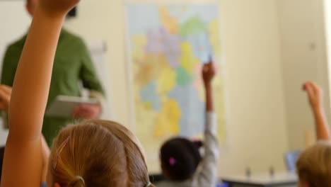 multi-ethnic schoolkids raising hands while sitting at desk in a classroom at school 4k